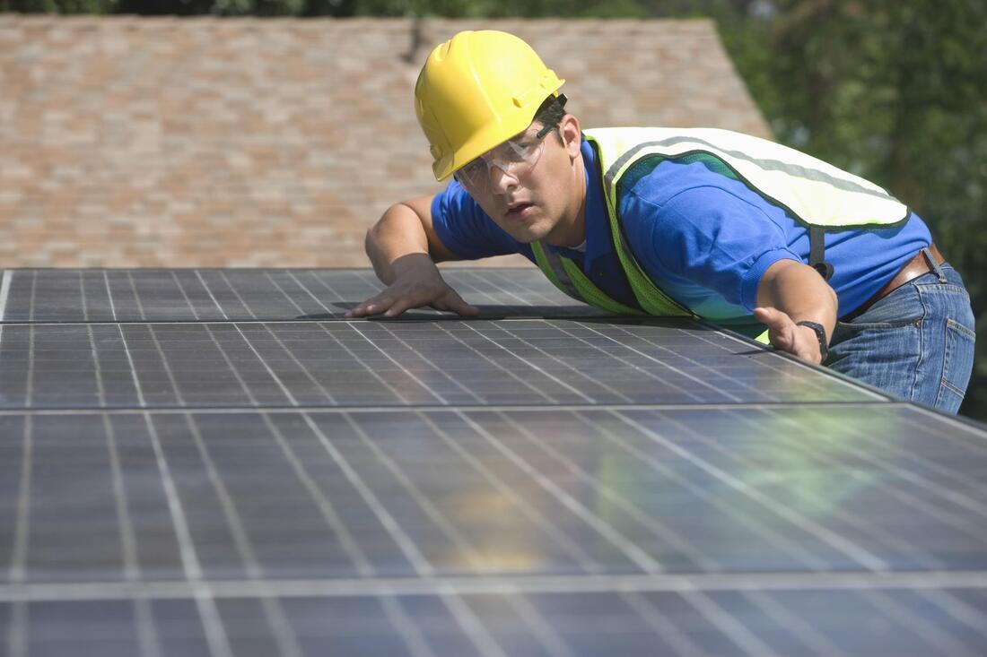 a man wearing a hard hat leaning over a solar panel
